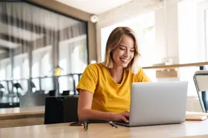 A woman sitting on a chair at a desk working on a laptop