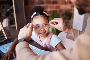A man is adjusting a young girl's glasses at a desk