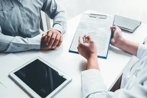 Two men having a conversation in an office setting, one of whom is holding a pen and paper