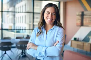 woman in an office with her arms crossed smiling at the camera