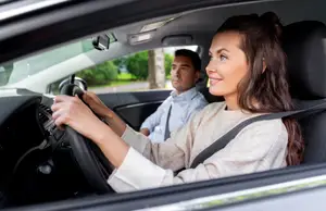 A woman is driving a car while a man sits in the passenger seat behind her.