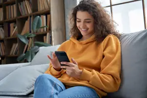 A woman sitting on a couch holding a cell phone and smiling