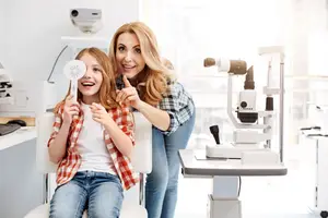 A woman and a girl are in an optometrist office, and the girl is holding a sun-like object with her finger pointing at it.