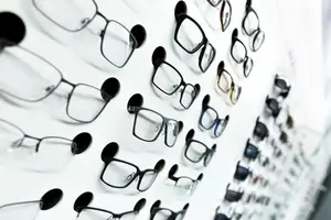 Multiple eyeglasses with black frames and clear lenses are displayed on a white wall.