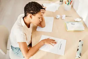 A girl is sitting on a chair and looking at a piece of paper on a desk with a pen in her hand