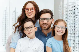 A family wearing glasses with a row of glasses behind them in a shop