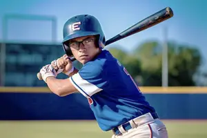 A baseball player in a blue jersey with the letter E on his helmet, holding a baseball bat and getting ready to hit the ball
