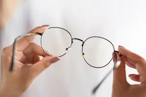 A person holding a pair of glasses in both hands