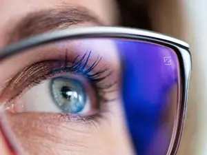 Close up of a woman wearing glasses with the reflection of a blue and purple background