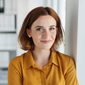 A woman wearing a yellow blouse is smiling and posing for a photo in a room