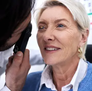 A woman with white hair is having her eyes examined by a doctor in a white shirt and a black eye phone