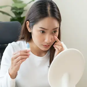 woman looking in mirror while holding a bottle of eye drops