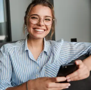 A woman in glasses and a blue and white striped shirt is smiling while looking at her phone.
