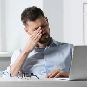 Business man with a headache covering his eyes with his hand while sitting at a desk