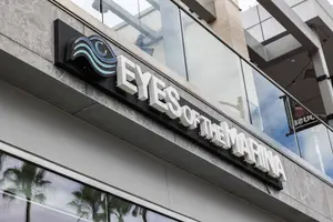Sign for Eyes of the Marina on a building with glass walls and palm trees in the background