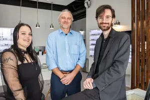 Three people posing for a photo in a shop with a white wall and hanging lamps