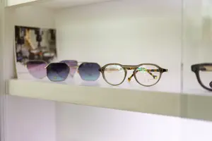 A white shelf with various pairs of sunglasses on display, featuring different colors and designs, placed inside a glass-fronted cabinet.