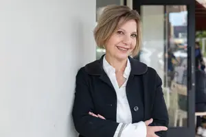 A smiling woman with short hair standing in front of a white wall with her arms crossed.