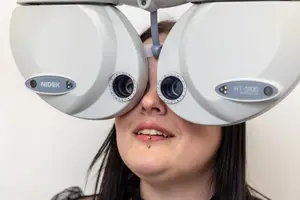A woman with long black hair is wearing a white machine with the word Nidek on it and looking into it.