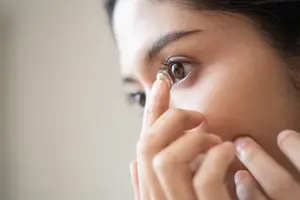 A woman is wearing a contact lens in her eye and seems to be posing for a photo.