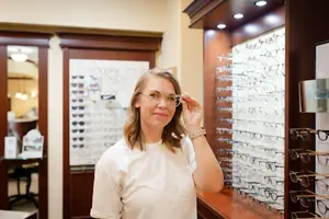 A woman in a white t-shirt is adjusting her glasses in front of a display of glasses