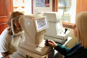 An eye test is being performed by a female technician on a female patient