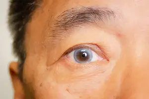 Close-up of a male human face with a blue eye looking at the camera and some wrinkles on the skin