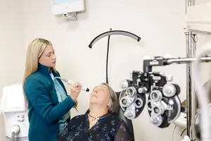 A woman is having her eyes examined by another woman in a medical office.