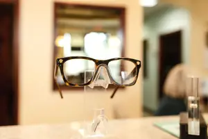 A pair of glasses is displayed on a clear glass stand in a room.