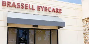 Brassell Eyecare clinic exterior with a grey awning over the entrance and a logo featuring an eye symbol and the text 'Brassell Eyecare' written in red on a white background