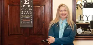 A woman wearing a blue coat is standing in front of a wooden door with an eye chart on it.
