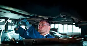 A mechanic wearing protective glasses and gloves working under a car in a garage
