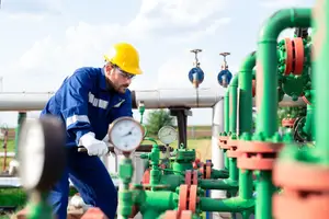A man in a blue uniform and a yellow helmet working on pipes at a factory