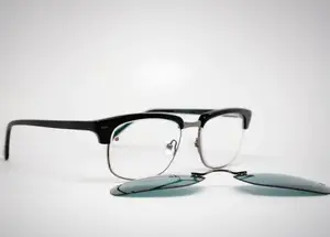 A pair of black-framed glasses with clear lenses and a small piece of green material lying beside them on a white surface