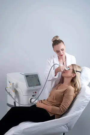 A woman is receiving laser treatment for wrinkles on her face while lying down on a bed in a room.
