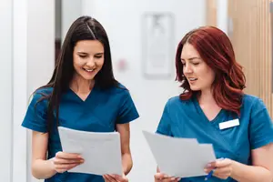 Two women with blue uniforms are standing and looking at papers