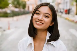 An Asian woman is smiling and posing for a photo on a sunny day.