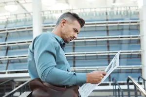 A man is walking down a flight of stairs while reading a newspaper