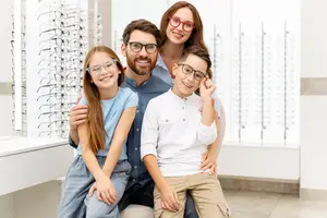 Four people wearing glasses are sitting together in a store and smiling at the camera