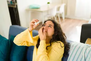 Woman sitting on a couch and putting eye drops in her eyes.