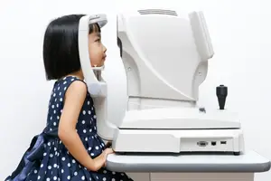 A young girl is sitting in front of an eye examination machine in an ophthalmology clinic.