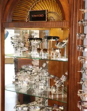 A wooden cabinet with multiple shelves and glasses on display. The sign on top says 'TOM FORD'.