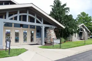 The entrance of the Sattler Nail Eye Care with a grassy lawn, a stone pillar, and a stone house on the side.