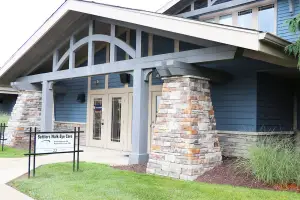 The entrance of Settlers Walk Eye Care building with blue walls and white trim, featuring a glass door and a signboard on the lawn.