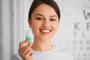 A smiling woman holding a white and green object, possibly a toothbrush, in front of an eye chart.