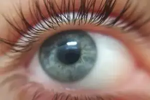 Close-up view of a person's eye with long eyelashes and a bright light reflecting off the eyeball.