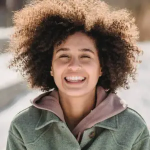 Woman with a curly afro hairstyle smiling in a winter setting