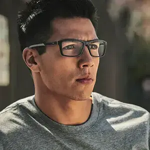 Man wearing glasses and a gray shirt posing for a photo with a blurry background.