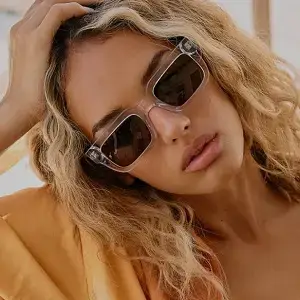 Woman with blonde wavy hair wearing sunglasses and a peach top looking down