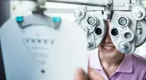 A woman wearing an eye test machine is smiling and posing for a photo